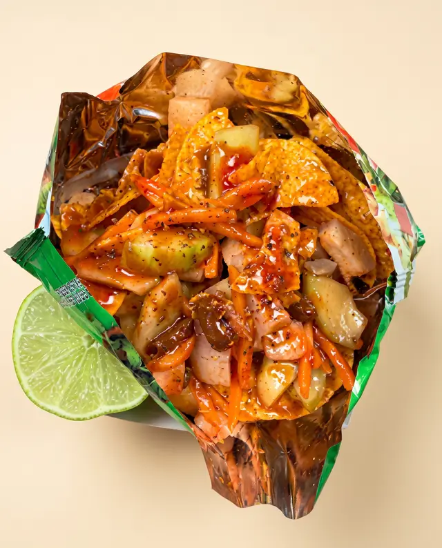 Una bolsa de Tostilocos abierta y cargada de cueritos, jícama, pepino y chamoy, con un gajo de limón