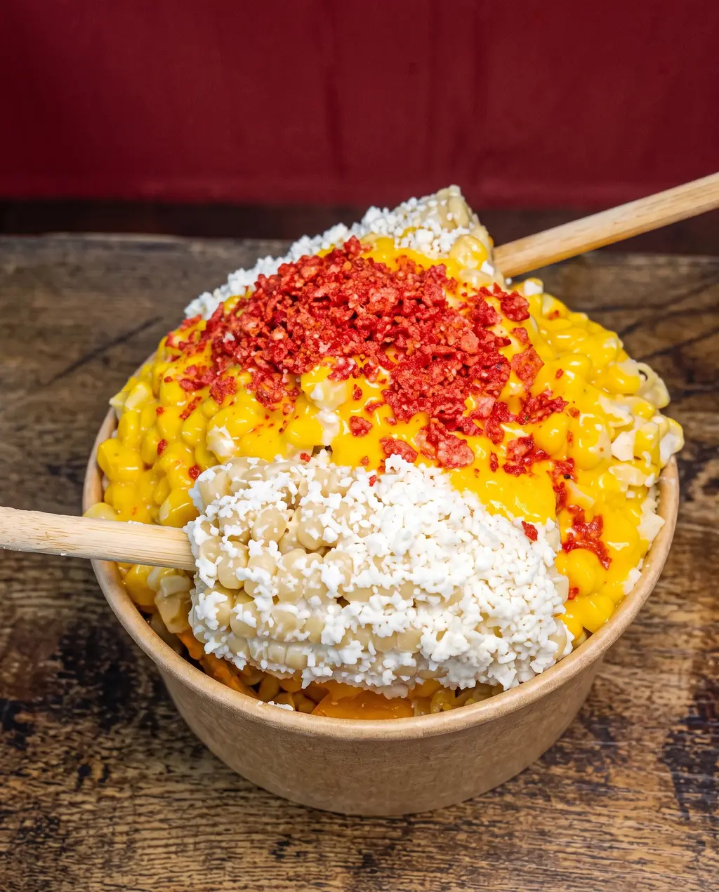 A cup of Poloco esquites: yellow corn buried under crumbled cotija and red chili