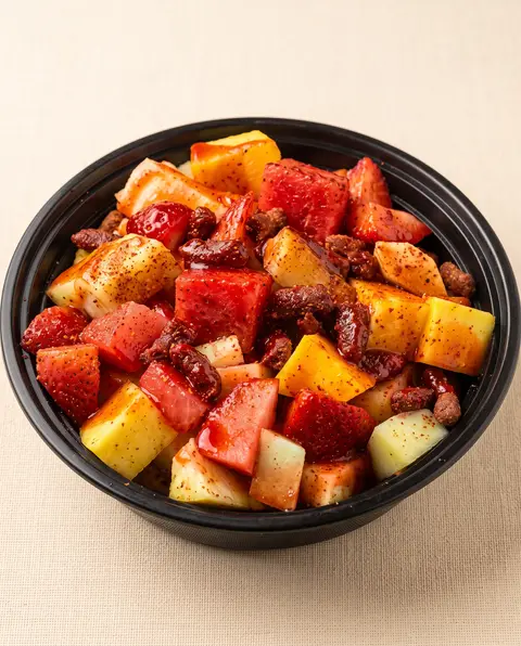 Un vaso de fruta con sandía, piña, mango y fresa bajo chamoy y chile en polvo