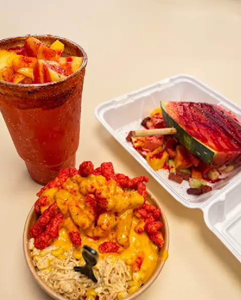 Un agua fresca escarchada con chamoy y mango, una charola de sandía y un tazón de ramen con queso y chips picantes