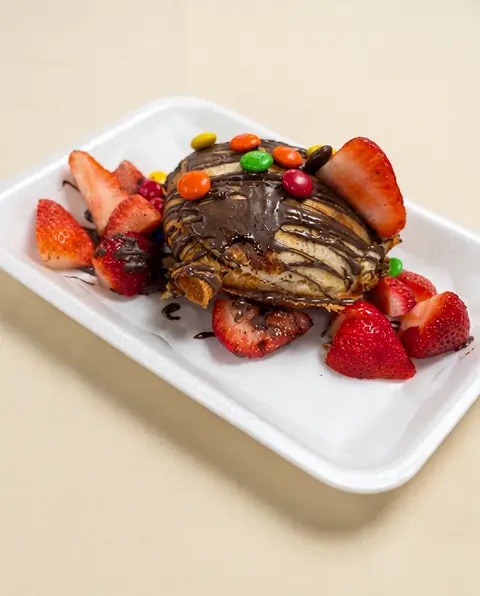 Un plátano cubierto de chocolate con chocolates de colores y fresas frescas