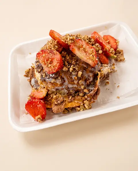 Un postre de churro cargado con caramelo, nuez picada y fresas rebanadas