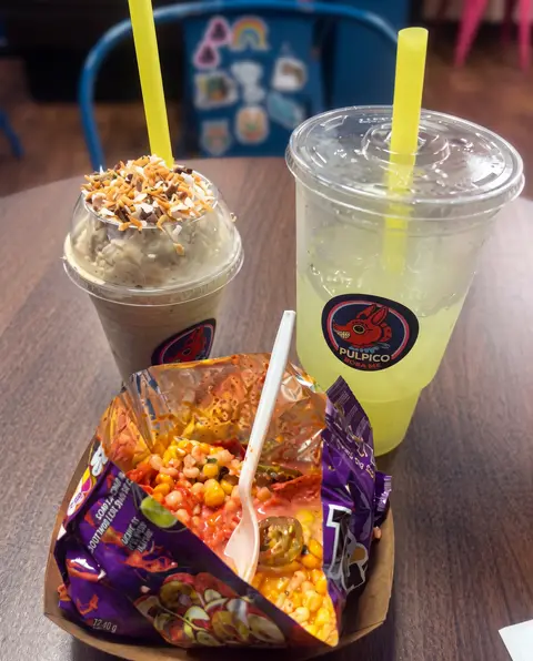 Un frappé y una limonada en vasos Poloco junto a una bolsa de chips cargada en la mesa de sillas azules