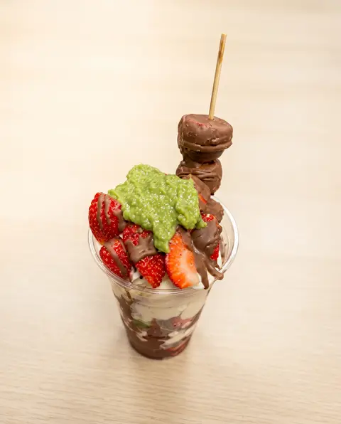 Un vaso de parfait con fresas, crema de pistache y un alambre de fresa con chocolate