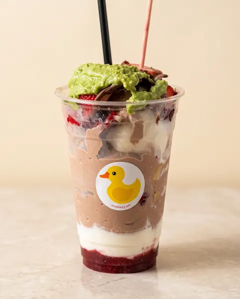 Un parfait en capas en vaso Poloco del patito: mora, vainilla y chocolate bajo crema de pistache