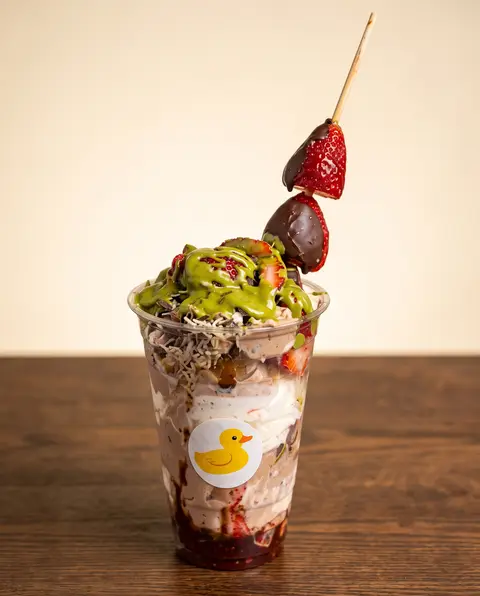 Un parfait alto en vaso Poloco del patito, con crema de pistache y un alambre de fresa con chocolate