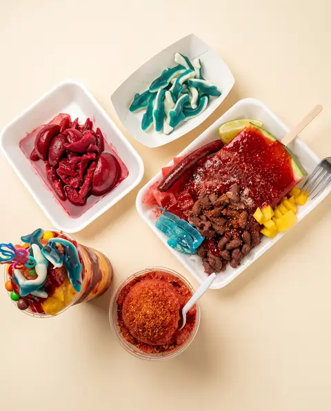 Los toppings de Poloco: cueritos, tiburones de goma azules, sandía con chamoy, un cono de nieve y un vaso de chamoy en polvo
